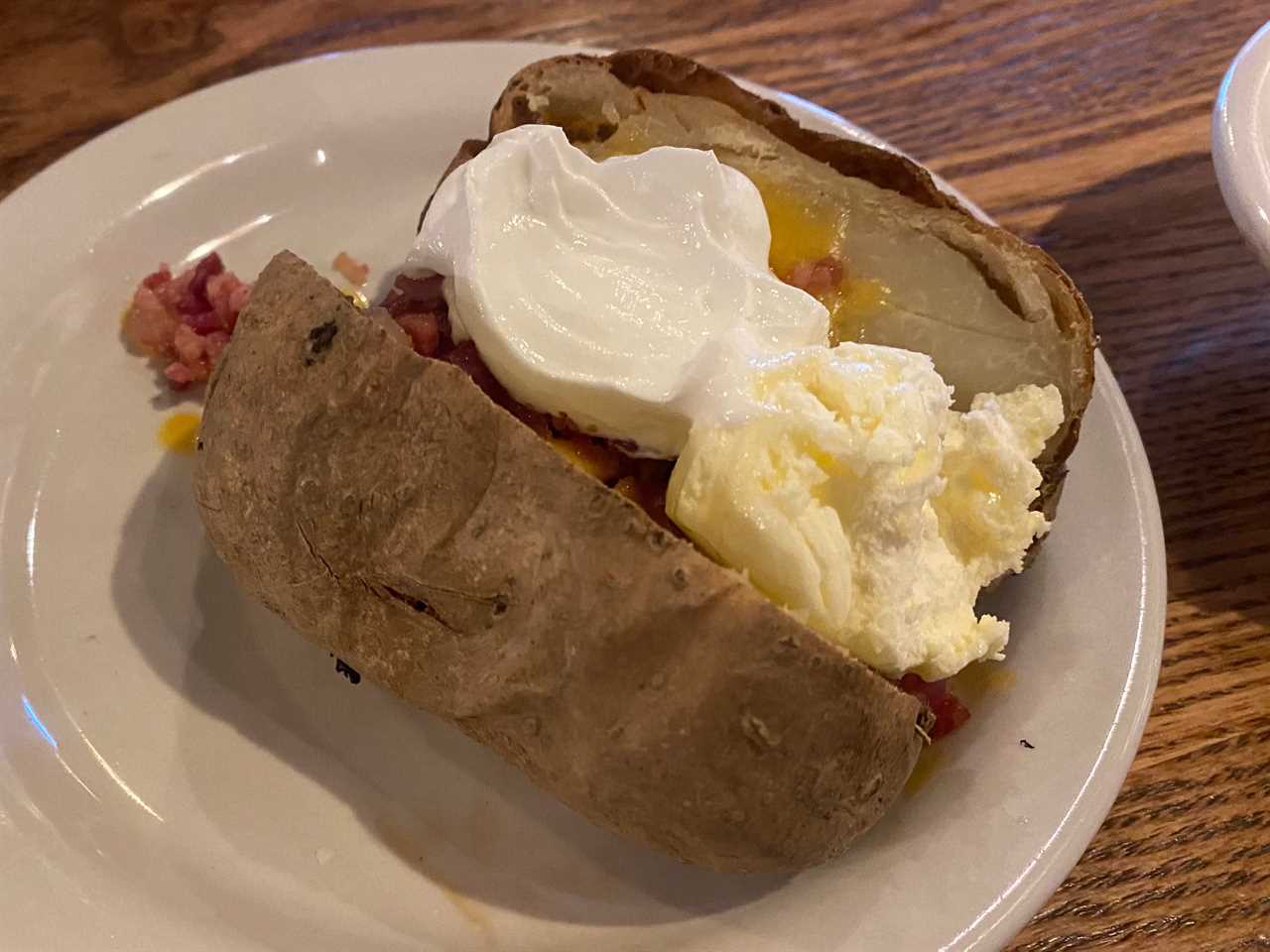 baled [otatoe with bacon bits, cheese, and sour cream on a plate at cracker barrel