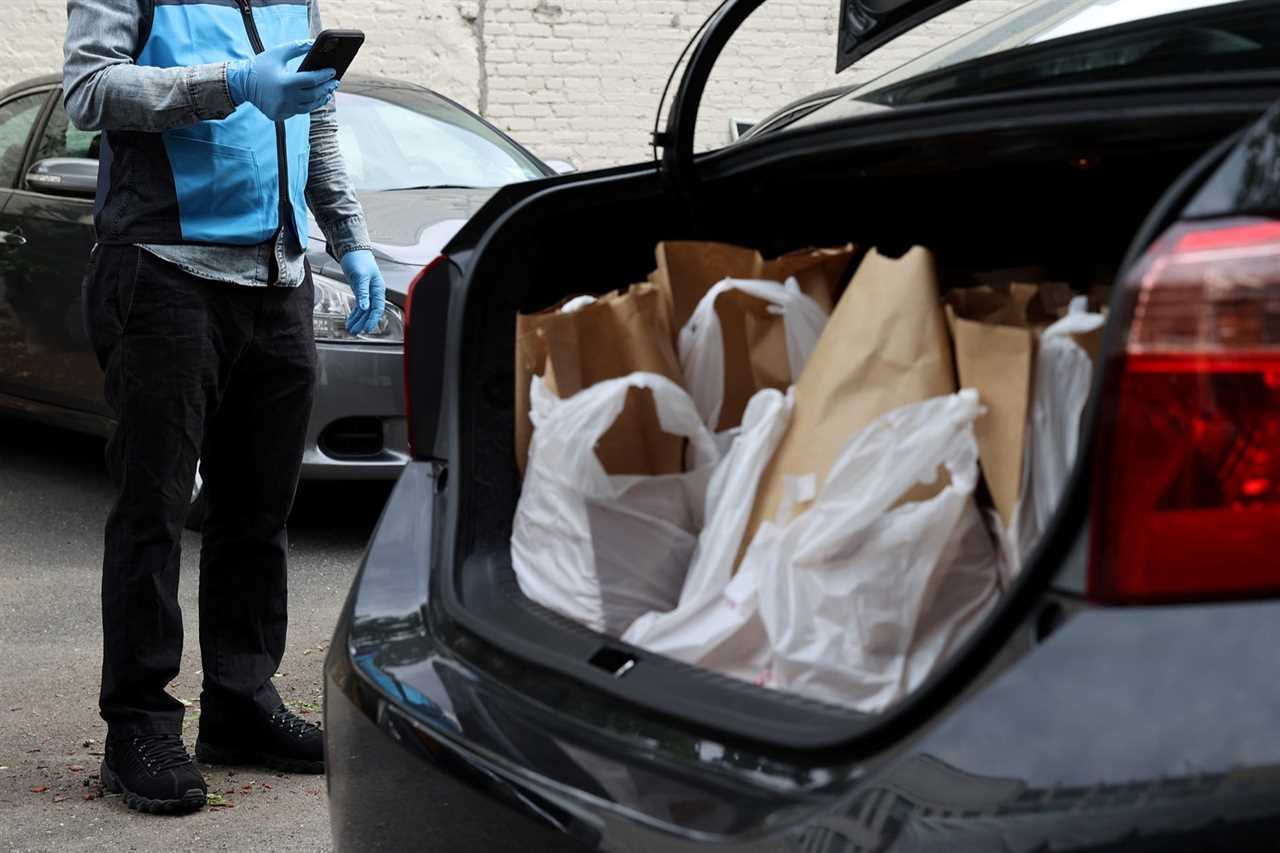 A delivery driver checks his phone near a trunk full of shopping bags.