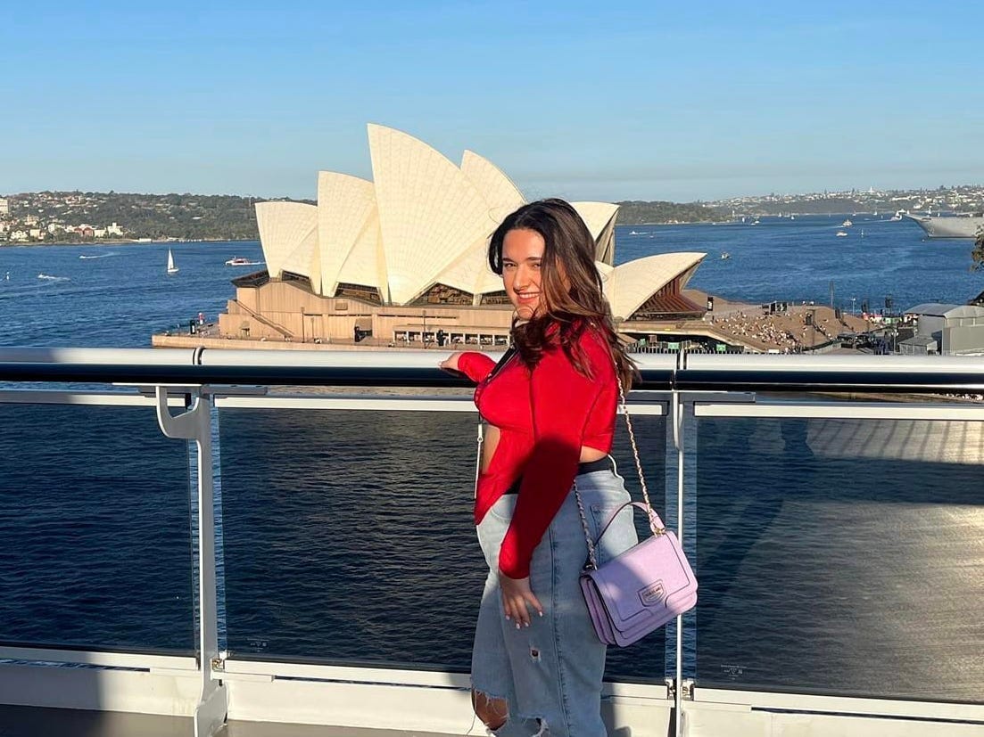 A woman stands in front of the Sydney Opera House