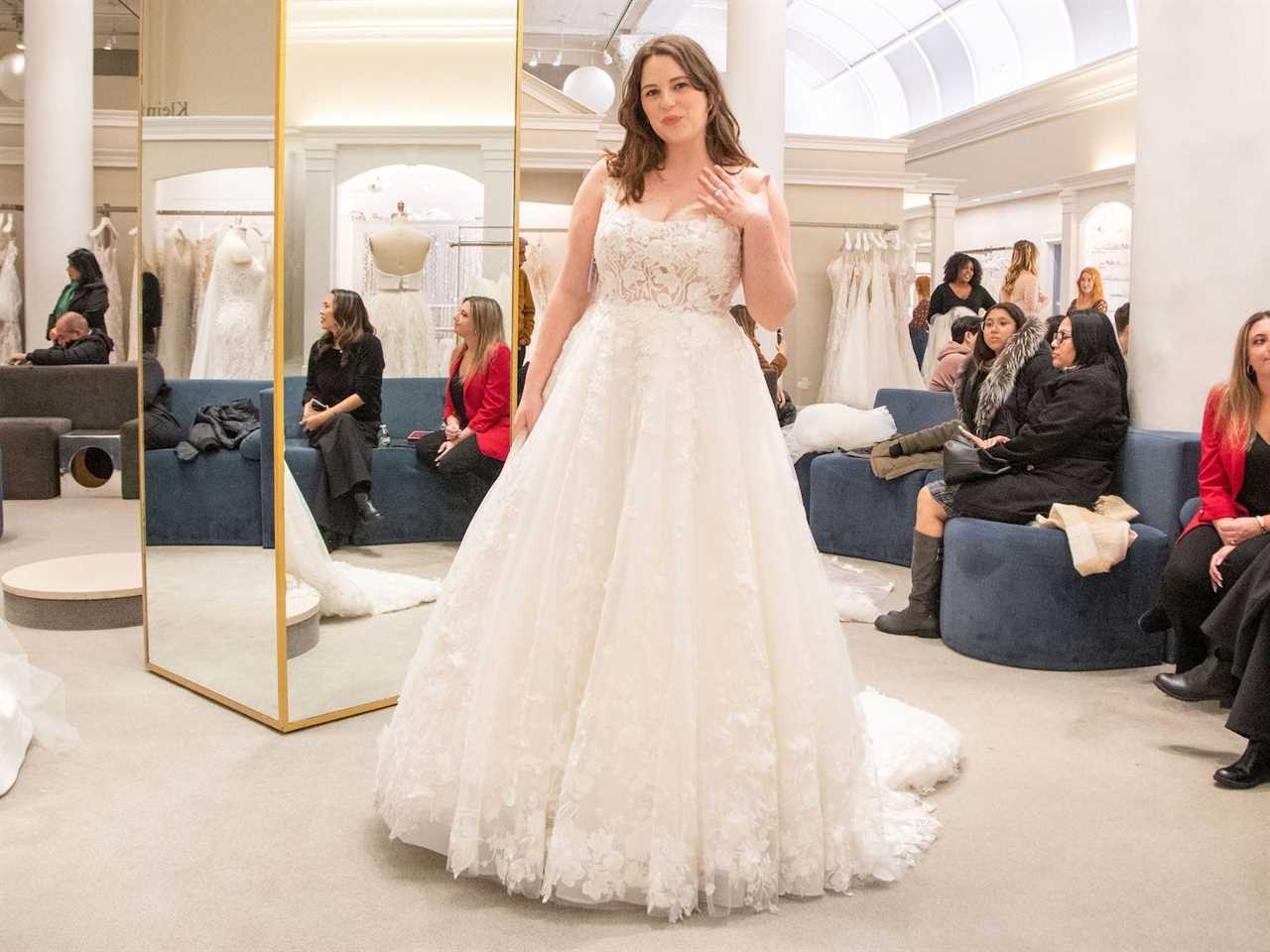 A woman stands in a wedding dress in a bridal boutique.
