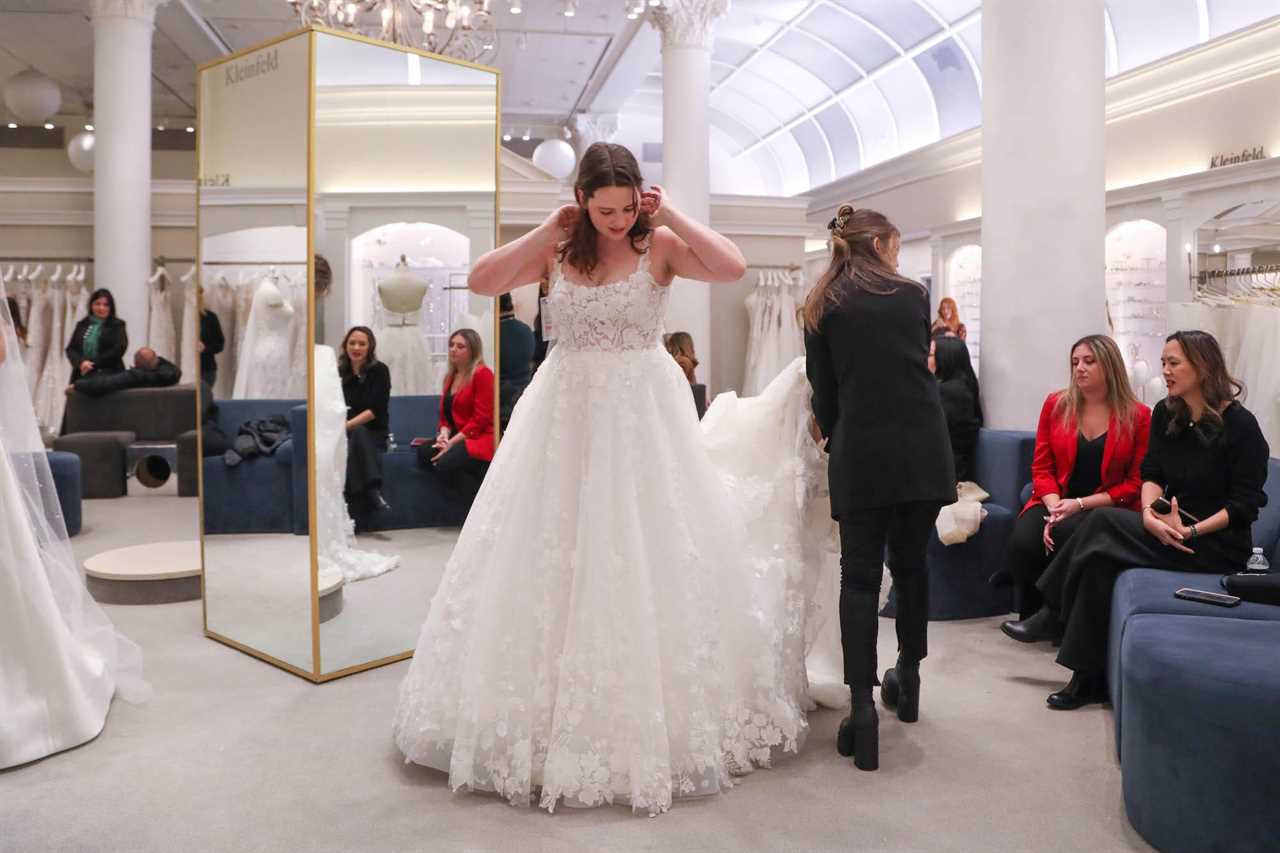 A woman looks down at a wedding dress she is trying on in a bridal store.