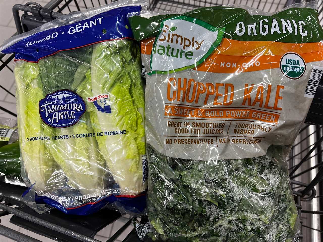 A bag of romaine lettuce and a bag of Simply Nature chopped organic kale in a grocery cart.
