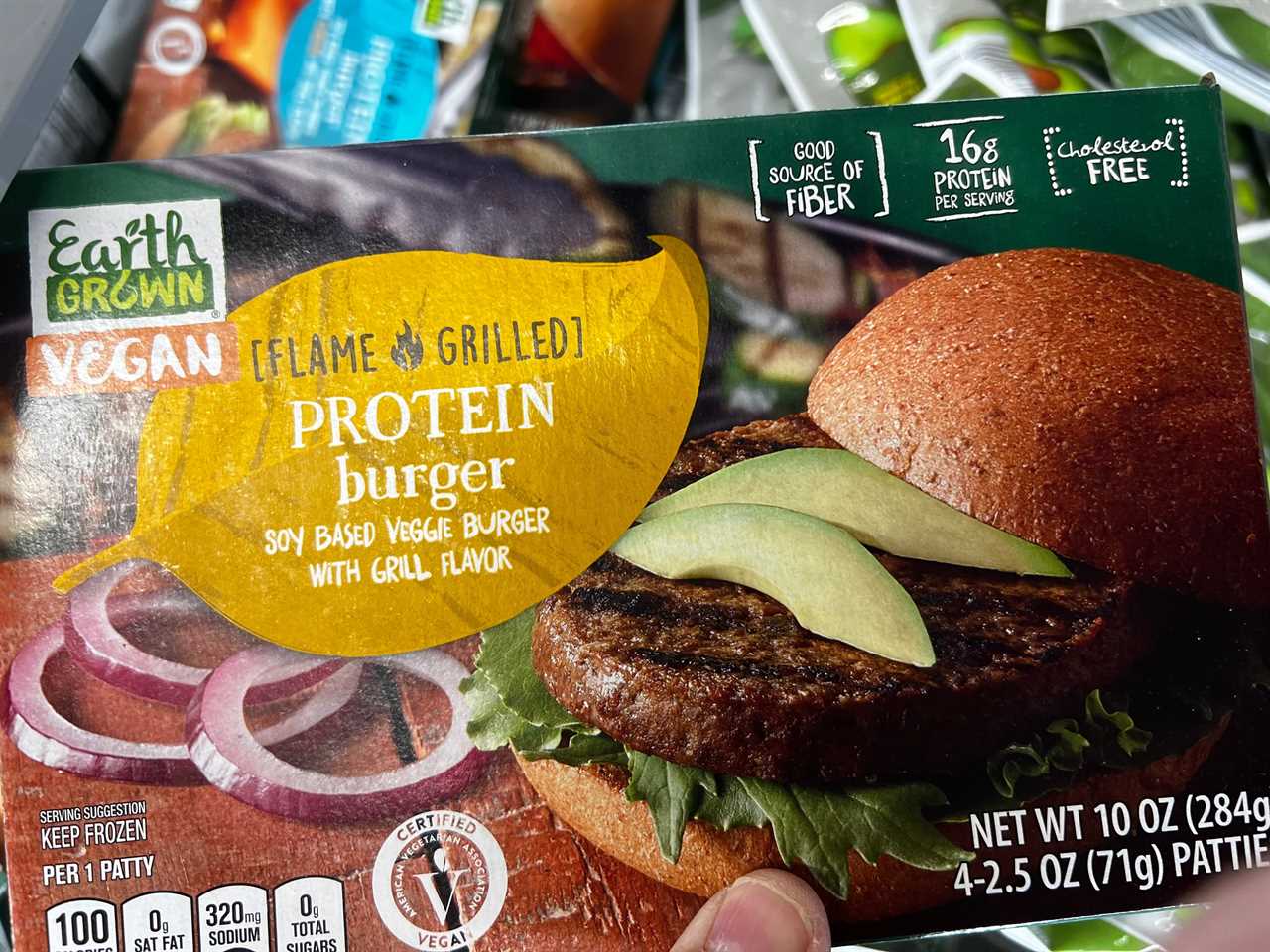 A hand holding a box of vegan flame-grilled protein burgers. 