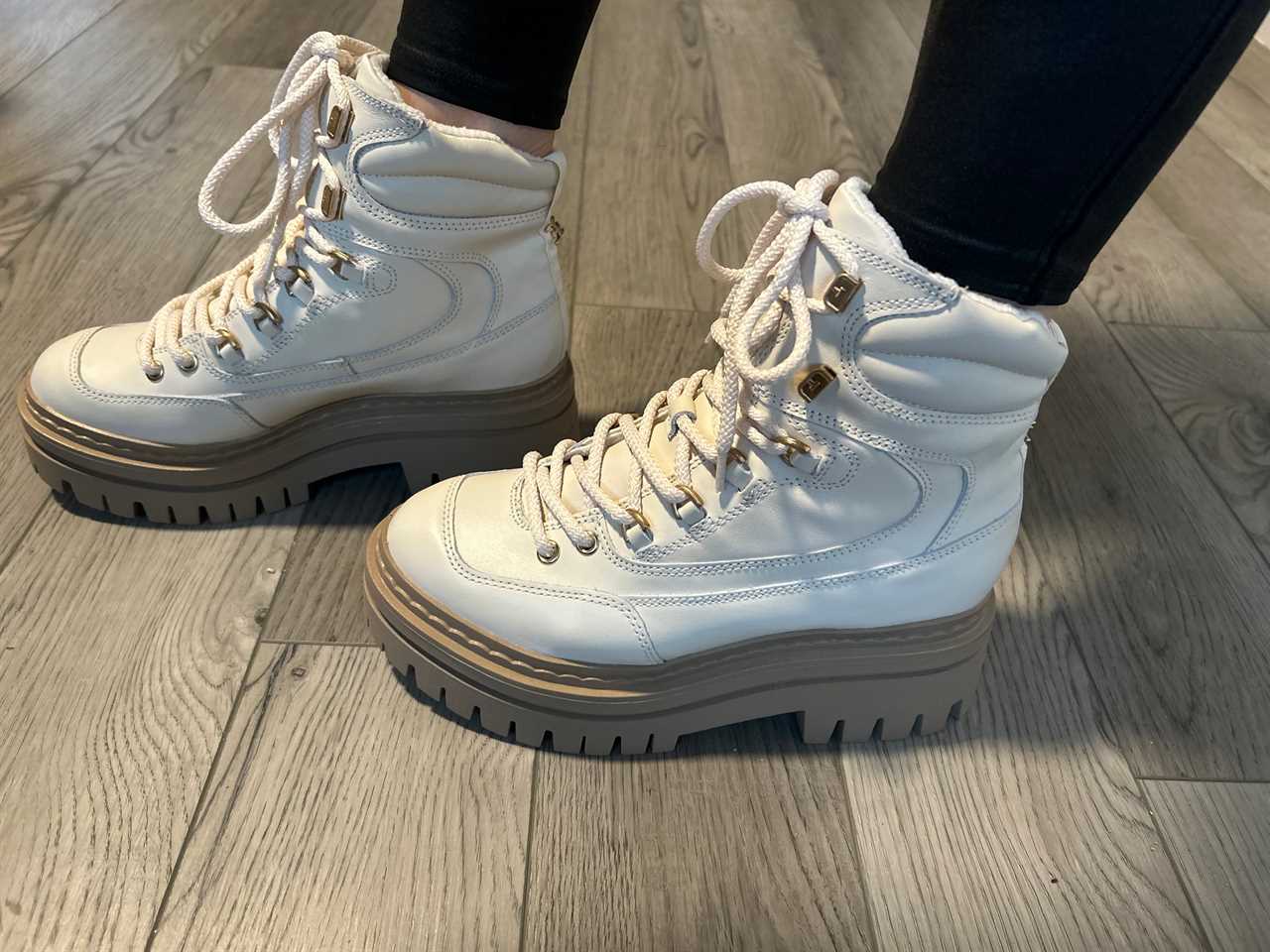 Person wearing Sam Edelman Kace Lace Up Lug Sole Boots in white while standing on wooden floor.