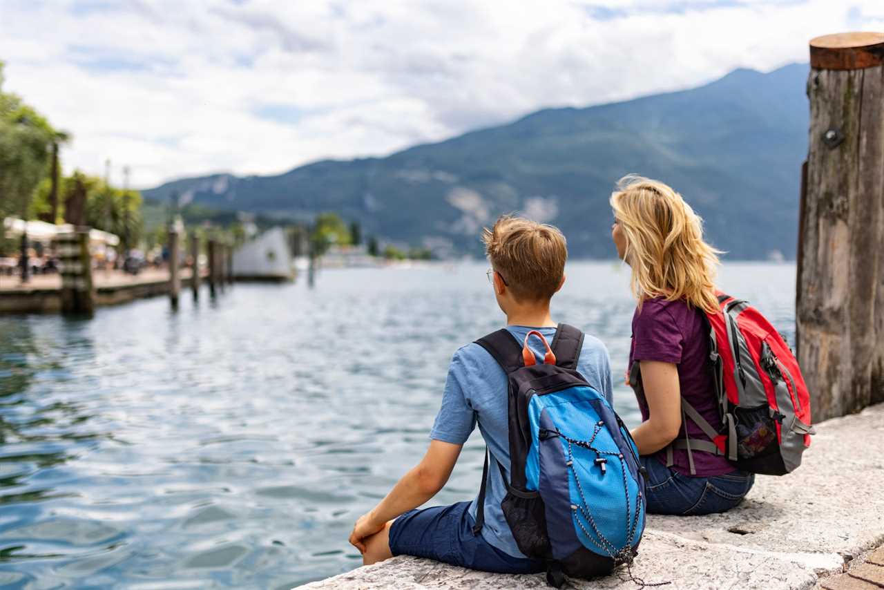 Woman and boy sitting on a dock wearing backpacks.