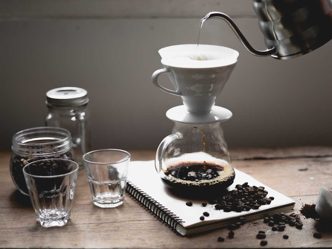 Brewing pour over coffee with spilled beans, several empty cups, and a jar of coffee beans.