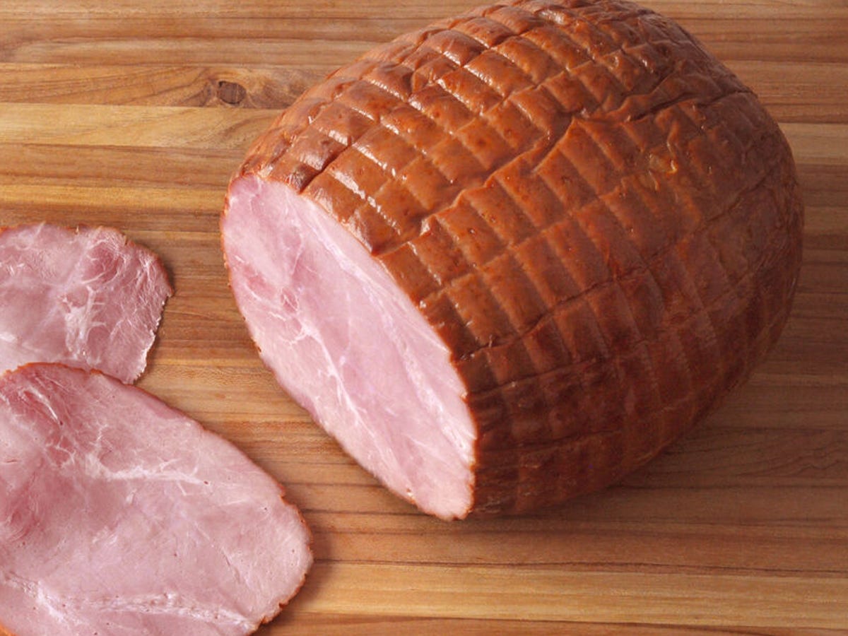 A partially sliced ham on a wood tabletop from D’Artagnan Berkshire Best Boneless Smoked Ham.