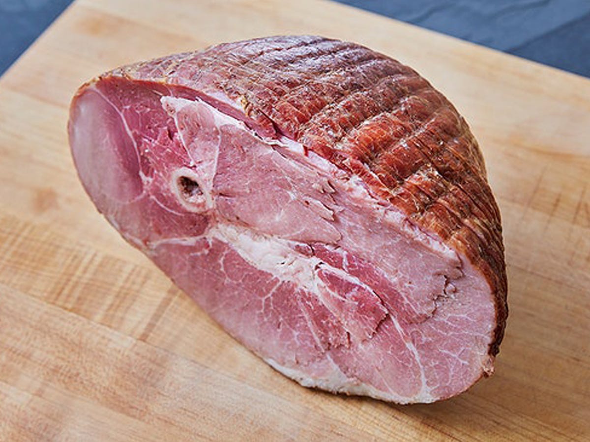 A cut half of a Crowd Cow Smoked Bone In Heritage Ham on a wood cutting board.