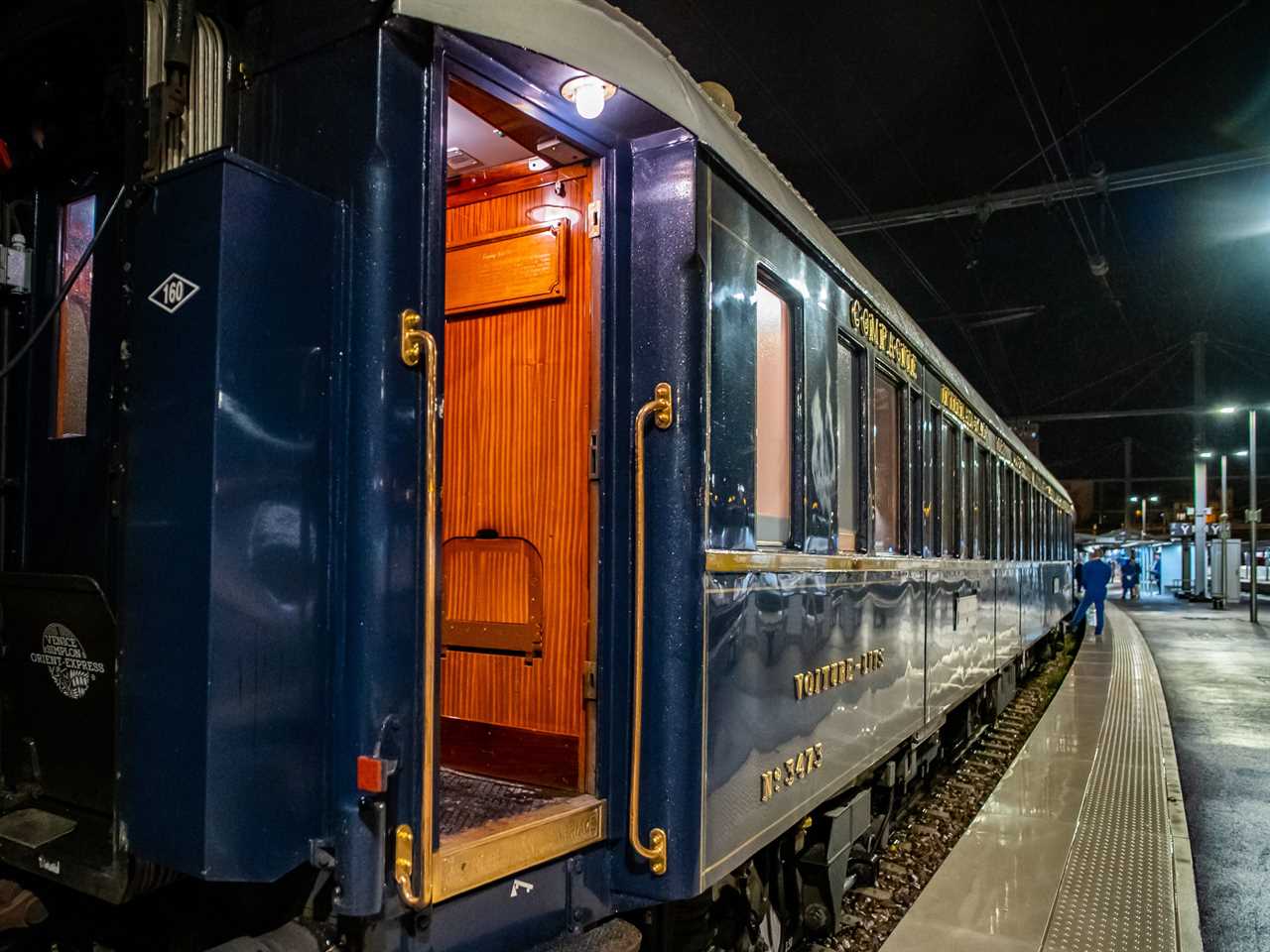 A navy blue luxury train parked at a platform at night.