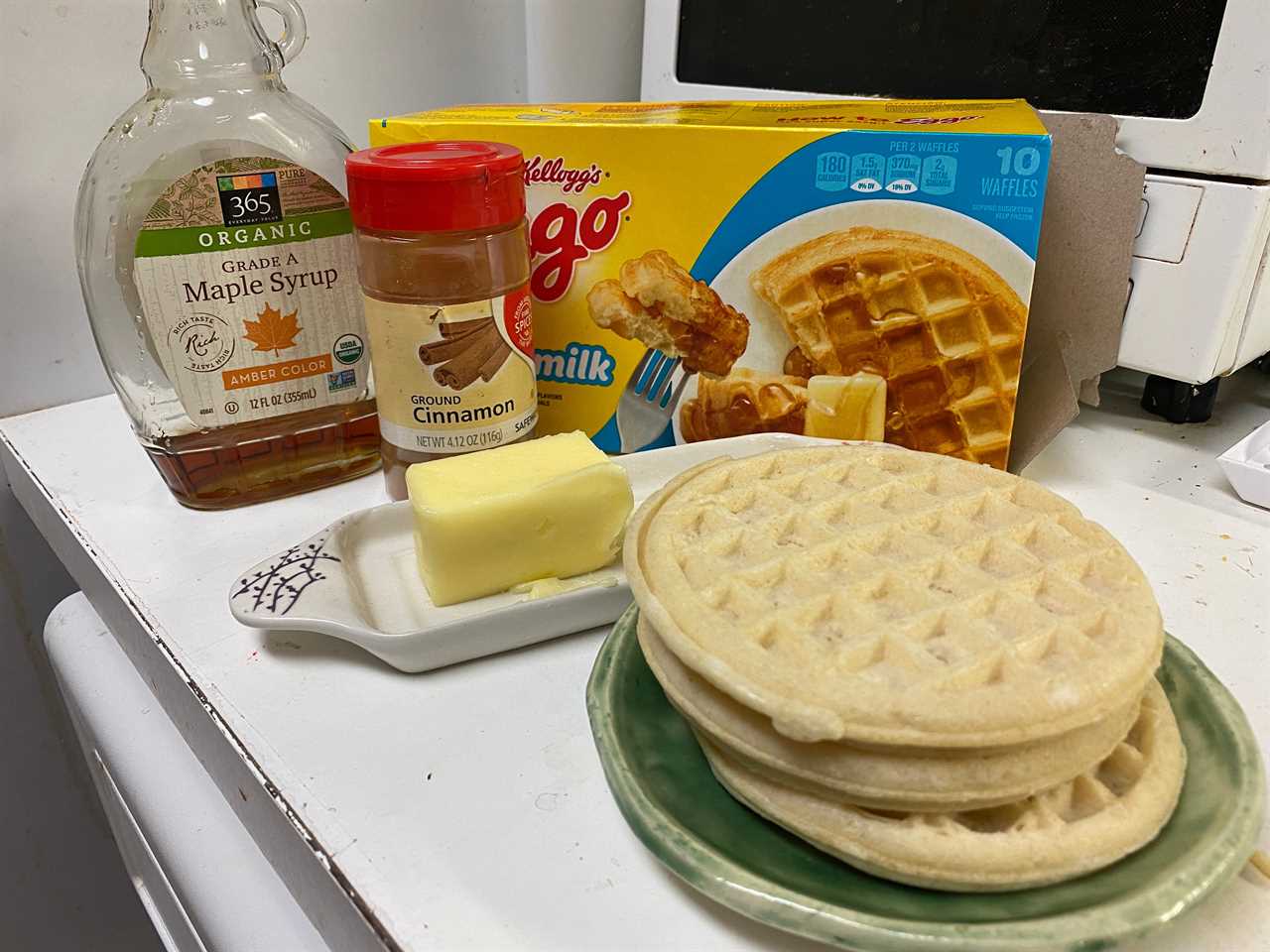 stack of frozen waffles in front of butter, cinnamon, syrup, and the waffle box on a counter