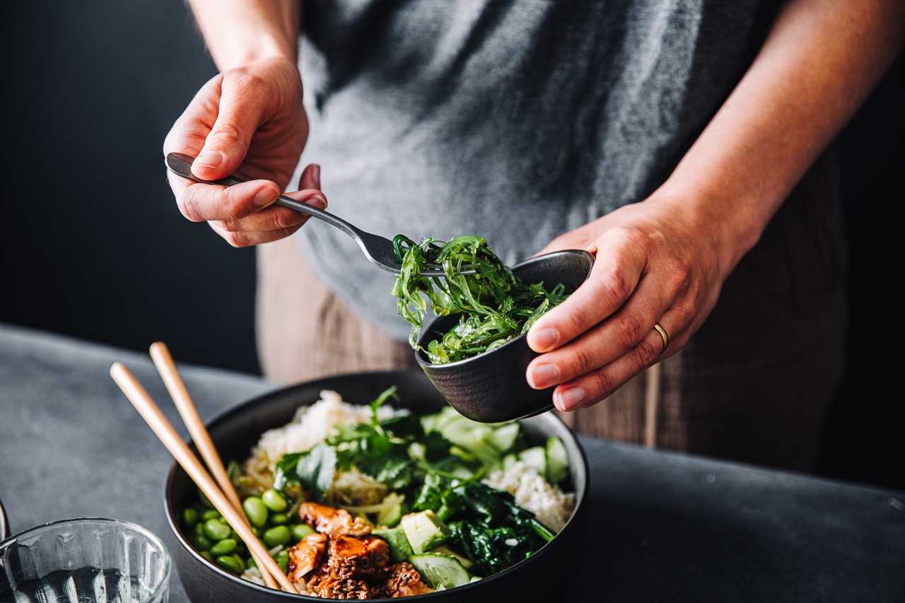 A person using a fork to put seaweed on a poke bowl.